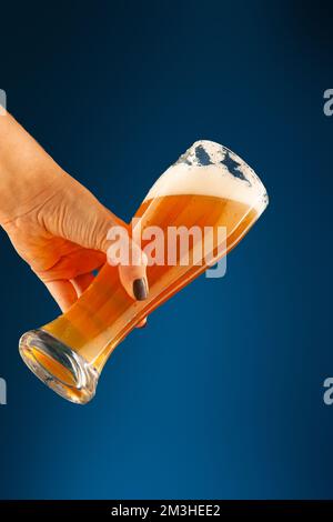 hand holds a glass with foam and bubbles on a blue background Stock Photo
