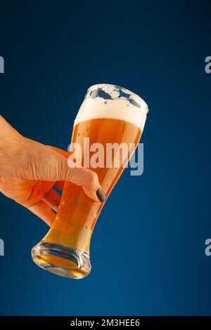 hand holds a glass with foam and bubbles on a blue background Stock Photo