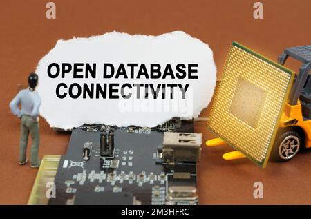 Computer concept. On the board with microcircuits lies a paper plate with the inscription - Open Database Connectivity. Nearby is a toy loader with a Stock Photo