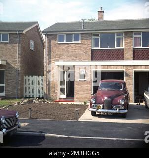 cira late 1960s, historical, a post-war maroon coloured Humber Hawk car parked in the driveway of a new semi-detached house, with an internal garage, built in the modern style of the era, as seen on many housing estates in Britain at this time. The Humber Hawk was a car built in Britiain by Humber Limited, between 1945 and 1967, with a number of different styles and variations. The car seen here is most likley the Humber Hawk Mark VI which was introduced in 1954 an upgraded version of the post-war 1948 Hawk, a completely newly designed car than the first and original 1945 Hawk. Stock Photo