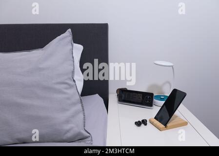 Smartphone on the bedside table with lamp, headset, clock and bed. Actual for the bedroom. Stock Photo