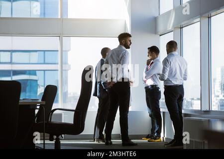 Silhouettes of people standing near a panoramic window in a modern office. Team of young professional business people working and chatting together in Stock Photo