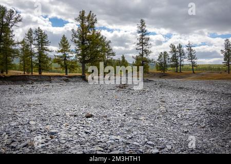 Dried up river bed in a rural countryside with the snowy mountains in the background. Majestic landscape with the rock road and hills. Stock Photo
