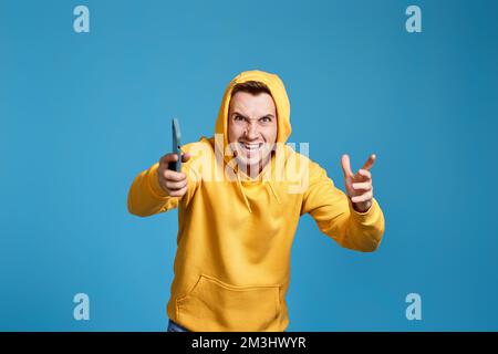 angry man in yellow sweatshirt holding mobile phone Stock Photo