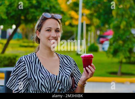 girl with refreshing drink in hand, behind green landscape Stock Photo