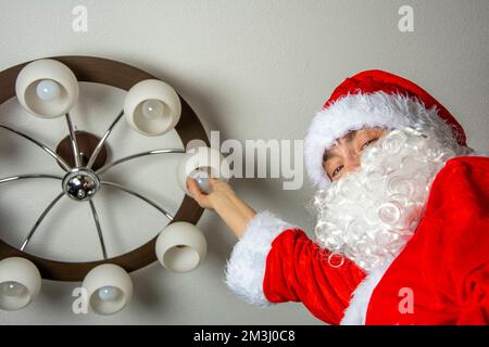 Santa changes the burned-out light bulbs in the chandelier Stock Photo