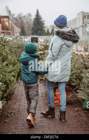 A young mother and her son are buying a Christmas tree. Outdoor Family Choosing Christmas Tree Together. Happy boy with his loving mother choosing fre Stock Photo