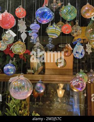 Hand blown decorative Christmas bulbs hang in a store window during the December holiday season. Stock Photo