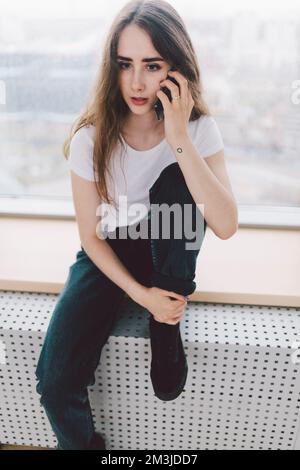 Surprised woman talking on the phone while sitting by the window Stock Photo