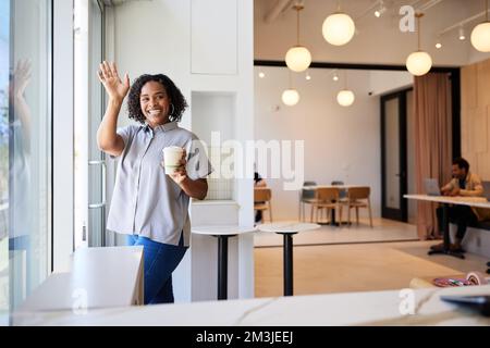 Happy woman with disposable coffee cup waving while leaving cafe Stock Photo