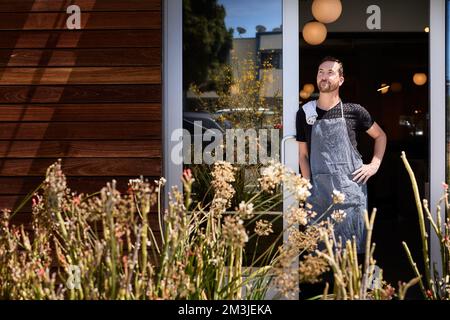 Contemplative male owner with hand on hip leaning at doorway in cafe Stock Photo