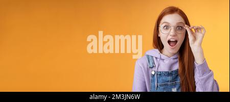 Omg so cool. Portrait amazed speechless excited redhead girl drop jaw amused stare camera surprised find out awesome product net touch glasses reading Stock Photo