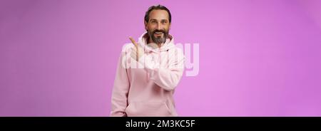 Good-looking lucky energized happy mature 50s man grey hair in trendy hipster hoodie pointing upper right corner amused telling you interesting news Stock Photo