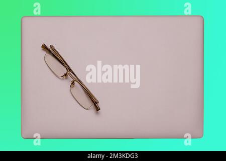 Modern silver closed laptop computer with eyeglasses on top Stock Photo