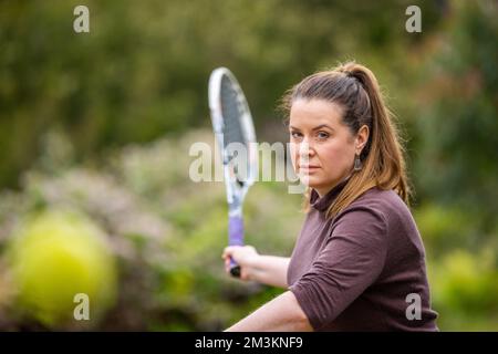 female tennis player practicing forehands and hitting tennis balls on a grass court in england Stock Photo