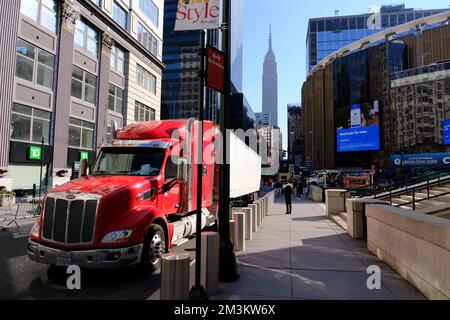 A red Semi-trailer truck parking on west 33rd street with Madison Square Garden and Empire State Building in the background.Midtown Manhattan.New York City.USA Stock Photo