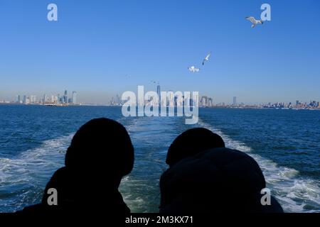 Passengers on Staten Island ferry with skylines of Jersey City, Manhattan and Brooklyn in the background.New York City.New York.USA Stock Photo
