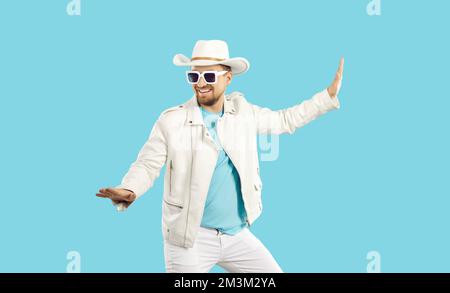 Funny man in white leather jacket, hat and sunglasses dancing isolated on blue background Stock Photo
