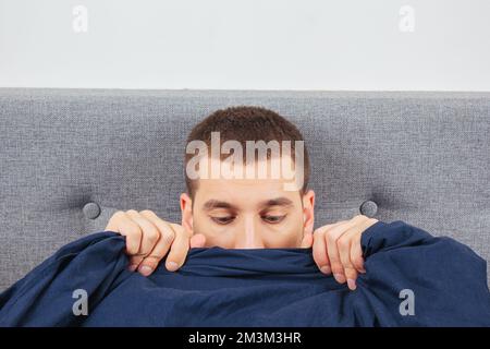 Look down. A handsome young guy hiding behind a blanket looks to the side. Direction of gaze in different directions. Stock Photo
