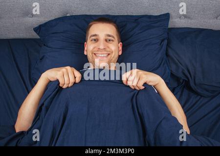 Looking straight into the frame. A handsome young guy hiding behind a blanket looks to the side. Direction of gaze in different directions. Stock Photo