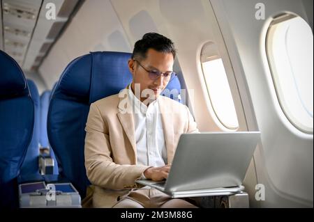 A professional and focused businessman or male CEO using a laptop computer, typing on the keyboard, managing his business tasks during the flight. Stock Photo