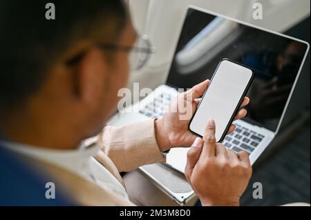 Smart and successful Asian businessman or CEO using his smartphone during the flight. close-up image of smartphone white screen mockup. Stock Photo