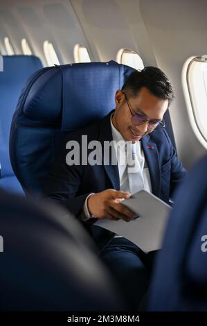 Portrait, Successful Asian businessman in formal suit reading business paperwork during the flight to his destination. Stock Photo