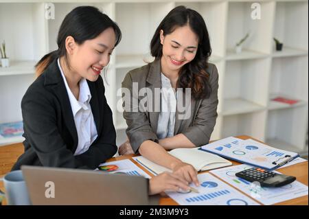 Two professional and focused Asian businesswomen or female financial analysts analyzing financial data on report, working together in the office. Stock Photo