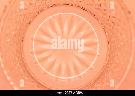 Macro abstract texture background of a round crystal glass surface with a sunburst design surrounded by diamond cuts, in the color of orange Stock Photo