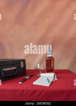wrist watch, bottle, glass, notebook, pencil, suitcase. Red tablecloth, brown background. retro Stock Photo