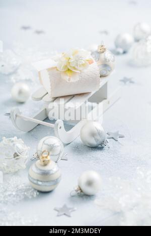 Christmas ornaments, balls and small present box on sledge in silver and snowy white Stock Photo