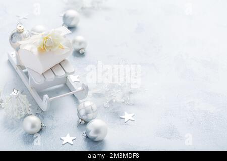 Christmas ornaments, balls and small present box on sledge in silver and snowy white Stock Photo