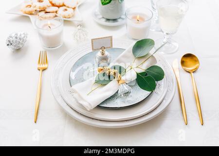 Christmas table setting with eucalyptus, cutlery and candles in white and green tone Stock Photo