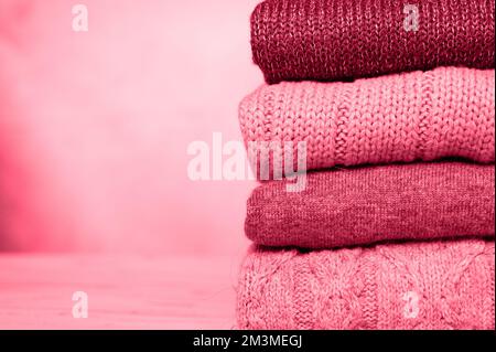 a stack of knitted winter sweaters in several shades of red pink purple. toned in viva magenta, trend color of the year 2023 Stock Photo