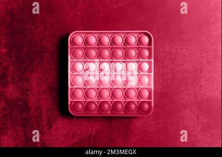 kids anti stress sensory pop it or simple dimple fidget push toy on a table. square popit red pink purple hue bright colo. top view, flat lay. toned i Stock Photo