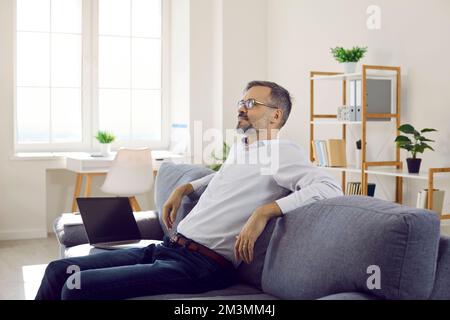 Mature businessman sitting on the couch and relaxing after working on his laptop Stock Photo
