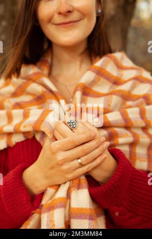 Cropped photo of young woman with dark hair wearing beige orange checkered warm scarf, rings, holding scarf with hands. Stock Photo