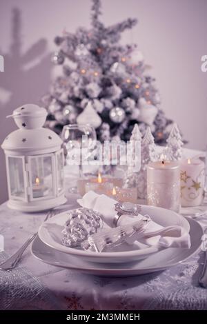 Festive  Christmas table place setting with silverware, candles and decorated Christmas tree Stock Photo