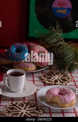 photo doughnuts lying in a pile on a plate next to them is a bitten off doughnut next to them is a cup on a saucer Stock Photo