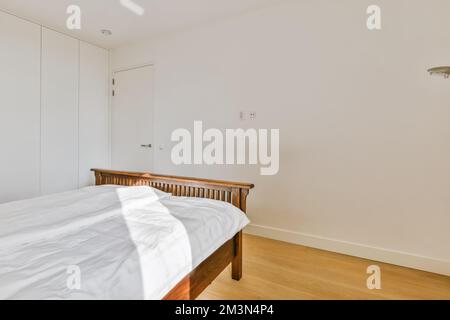a bedroom with white walls and hardwood flooring in the room, there is an empty bed on the right hand side Stock Photo