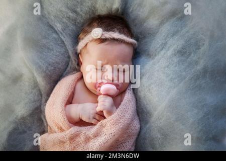 Portrait of sleeping newborn baby with dummy, swaddled in warm knitted blanket plaid. Child sucks pacifier nipple Stock Photo