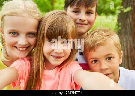 Happy group of children taking selfie photo with smartphone in nature in summer Stock Photo