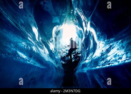 Silhouette of man hang on the rope climb and exploring amazing  blue glacial ice cave in the mountains in Kazakhstan Stock Photo