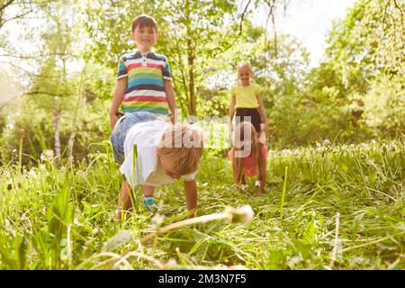 Playful boys and girls competing each other in meadow on sunny day during summer holiday Stock Photo