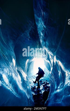 Silhouette of man hang on the rope climb and exploring amazing  blue glacial ice cave in the mountains in Kazakhstan Stock Photo