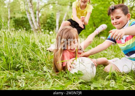 Group of children playing soccer and scuffling around football in grass at park Stock Photo