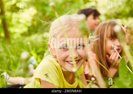 Portrait of smiling girl lying on front by female friend in meadow during summer vacation Stock Photo