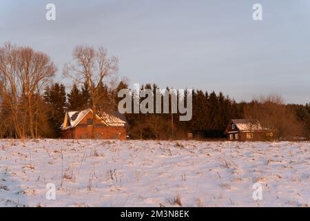 Winter forest and wooden houses in the evening in a snow-covered field, Kernave, Lithuania Stock Photo