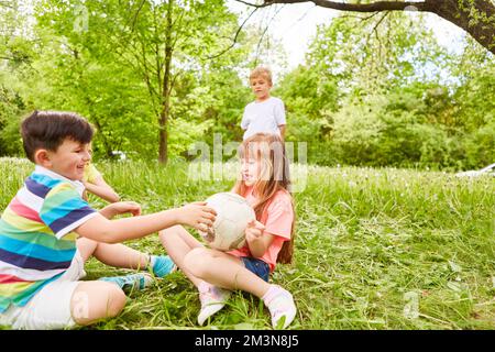 Happy boy and girl with soccer ball by male and female friends on grass at garden Stock Photo