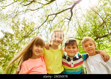 Portrait of smiling boys and girls with arms around standing in front of trees at garden Stock Photo